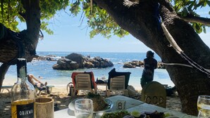 A table set for a meal with a bottle of wine, a glass of white wine, a plate of food, and a view of the beach and ocean. - Oasis Wadduwa (Wadduwa)