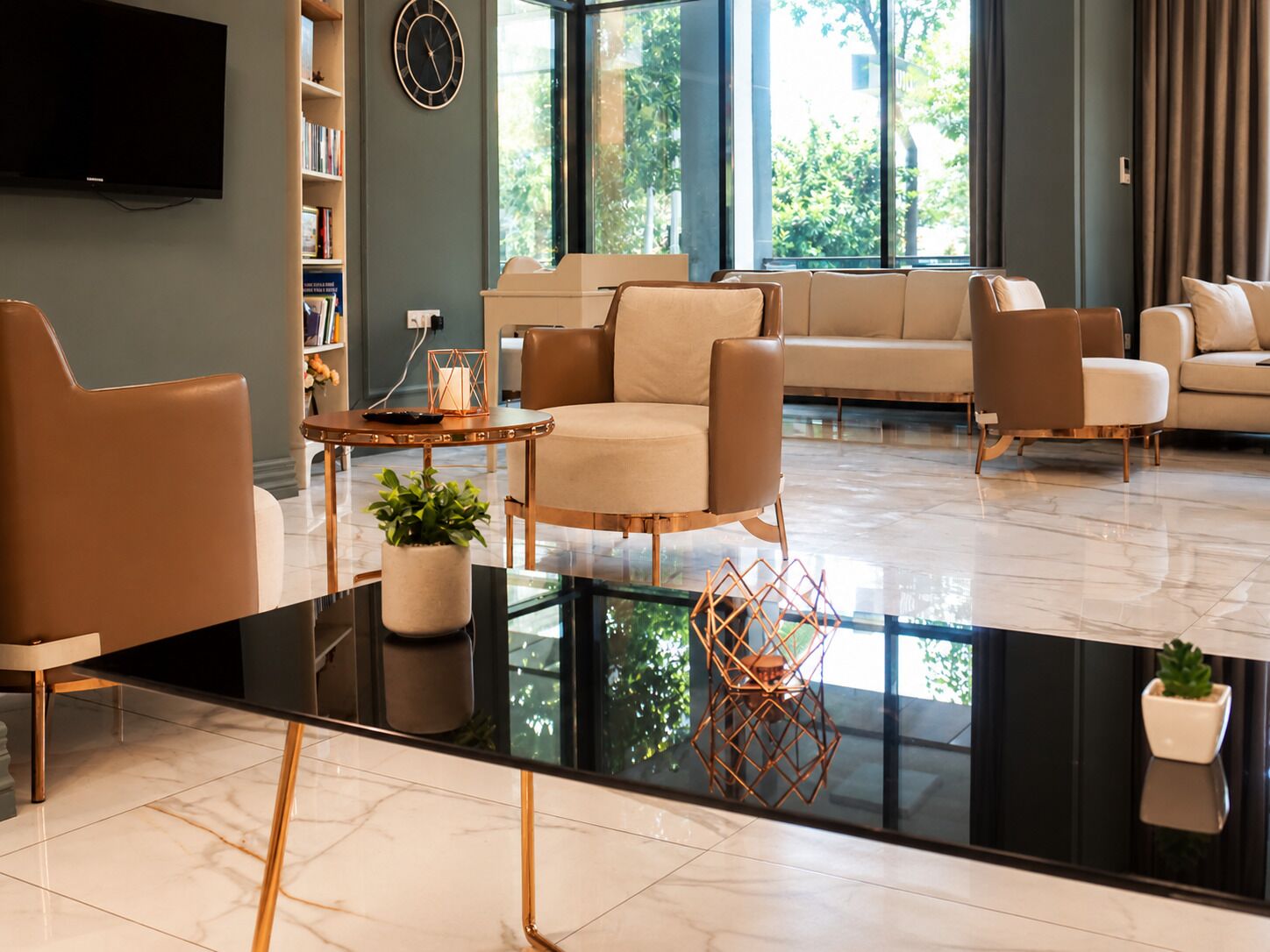 A modern living room with a black glass coffee table, beige sofas, and a large window with a view of greenery.