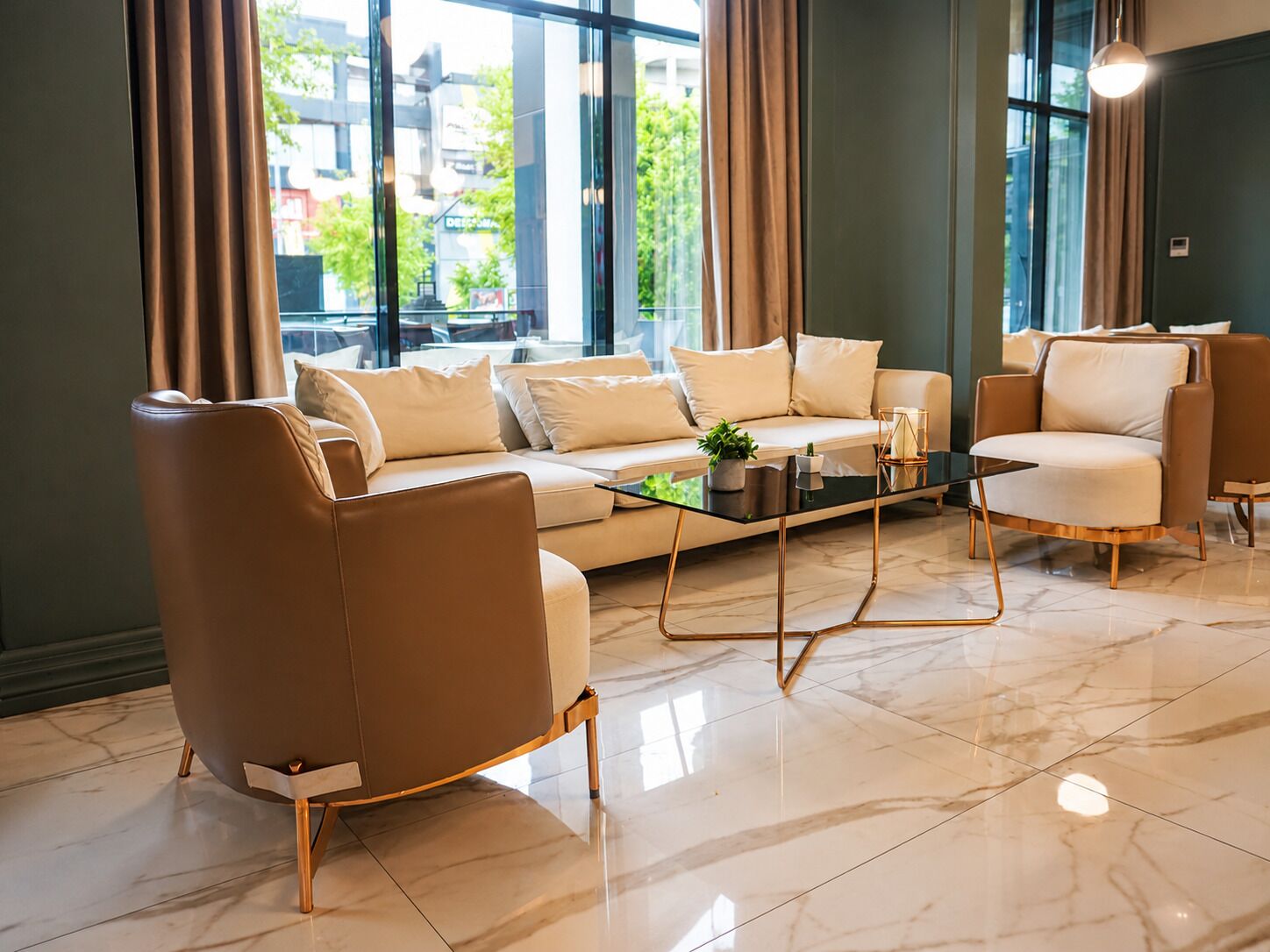 Ein modernes Wohnzimmer mit einer Couch, Sesseln, einem Couchtisch und großen Fenstern mit Vorhängen.