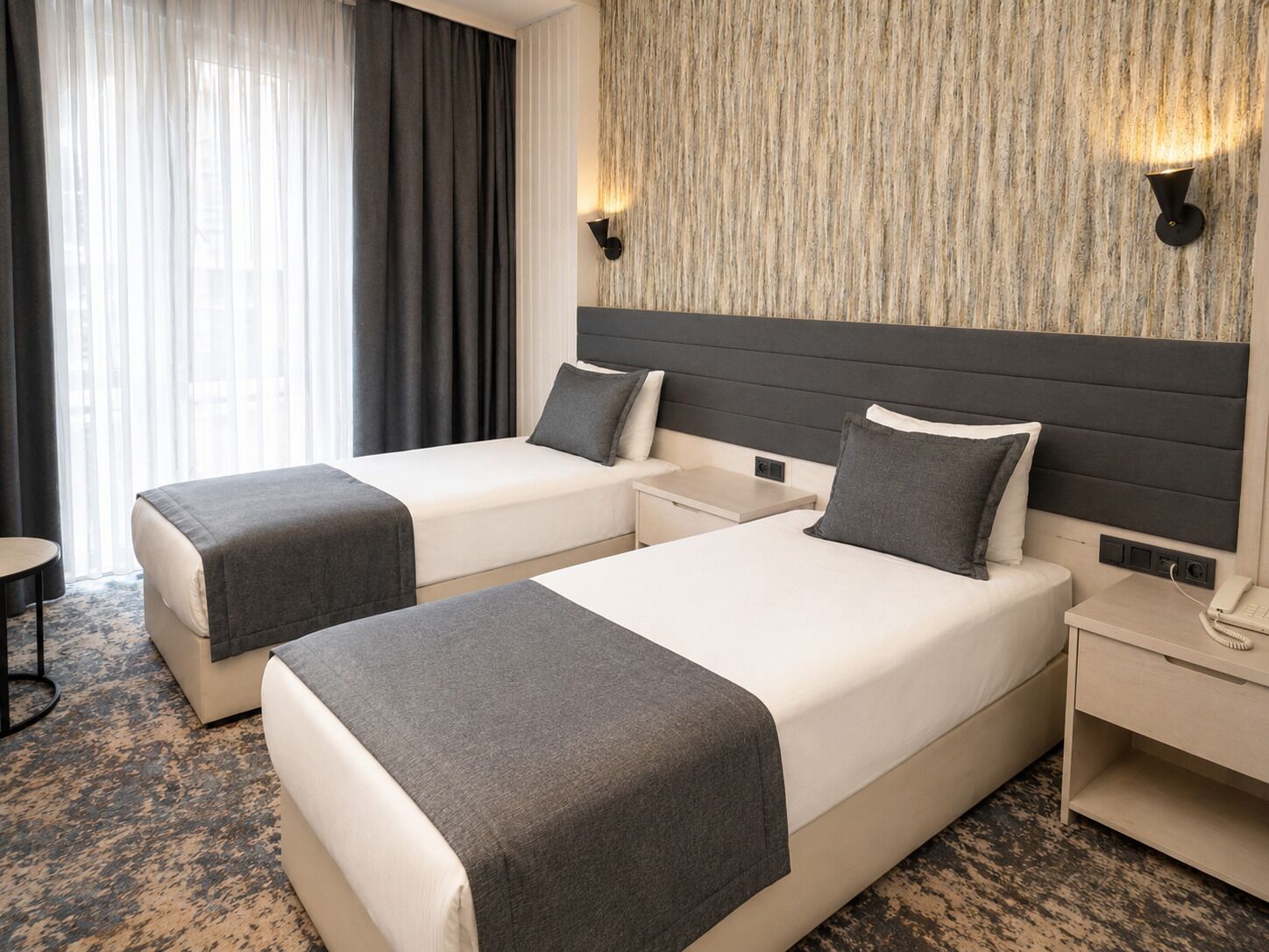 Habitación de hotel con dos camas, una mesita de noche, un teléfono y una lámpara fijada a la pared.