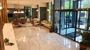 Eine großzügige Lobby mit Marmorboden, einem Essbereich, Sofas und großen Fenstern mit Blick ins Freie.
