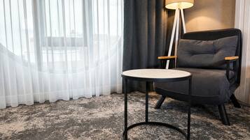 Una habitación con una mesa redonda, un sillón oscuro, una lámpara de pie y cortinas translúcidas.