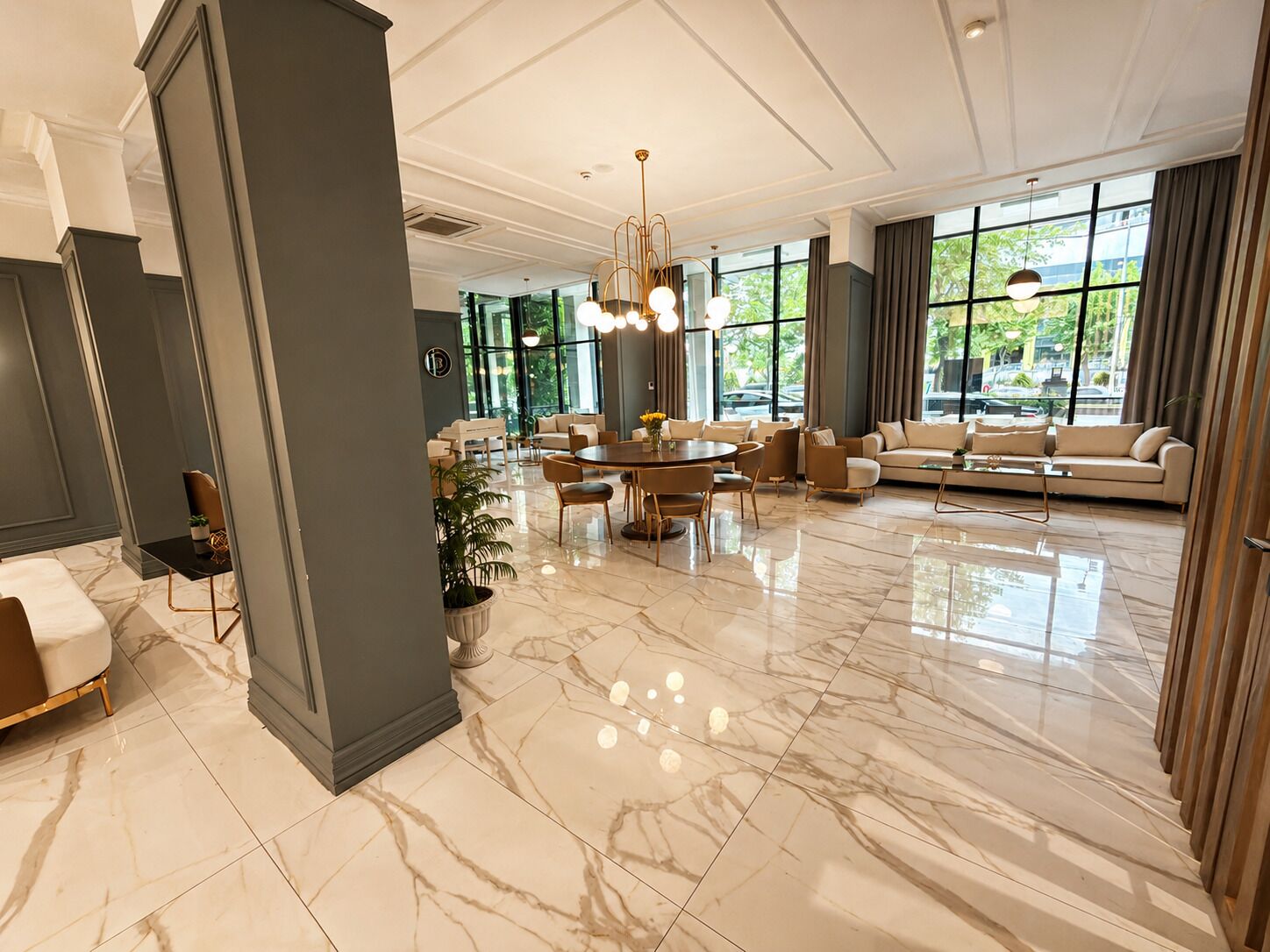Eine großzügige Hotelhalle mit Marmorboden, einem runden Esstisch, Sofas und großen Fenstern mit Blick ins Freie.