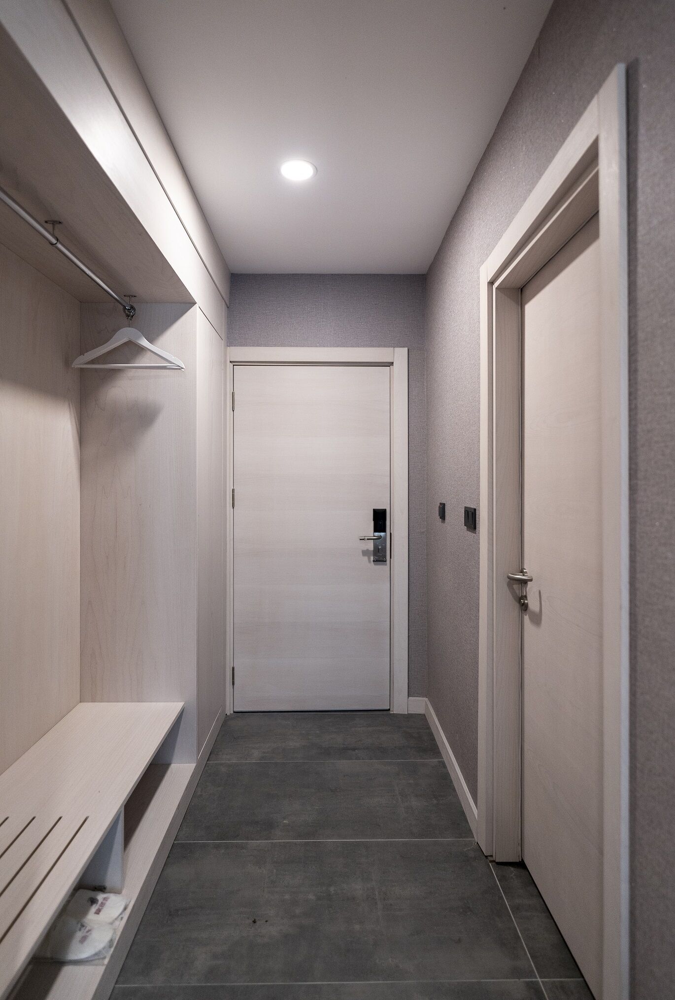 A narrow hallway with a bench, a coat rack, and a door at the end.