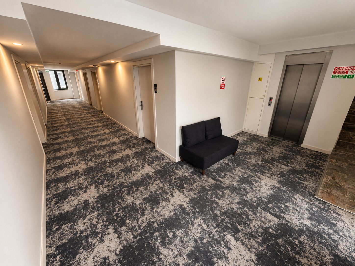 A hotel hallway with a black and white patterned carpet, a black sofa, and an elevator.