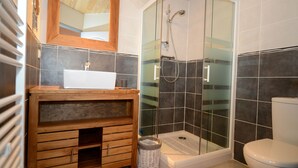 Un baño con tocador de madera, cabina de ducha de vidrio y inodoro blanco.