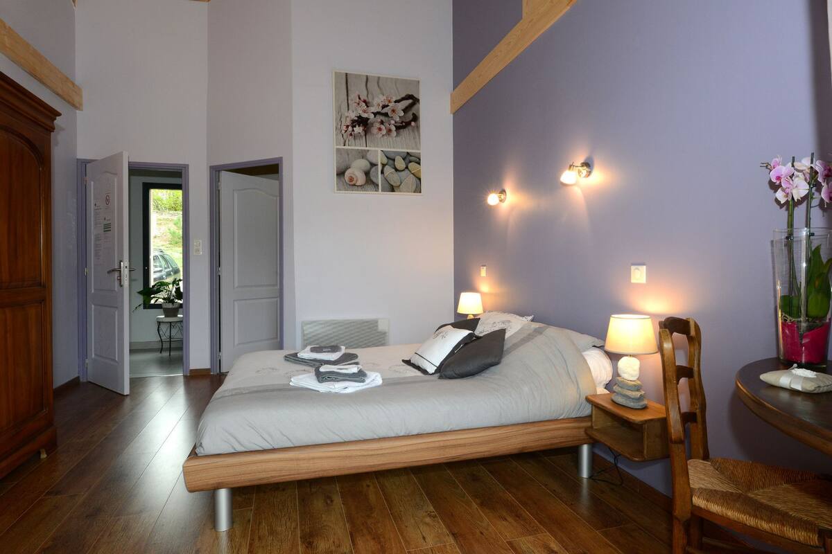 Een slaapkamer met een houten bed, twee nachtkastjes met lampen, een houten stoel, een houten kledingkast en een deur die leidt naar een balkon.