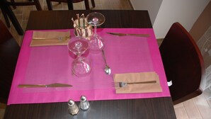 Una mesa de comedor puesta con mantel rosa, cubiertos, una copa de vino y saleros y pimenteros.