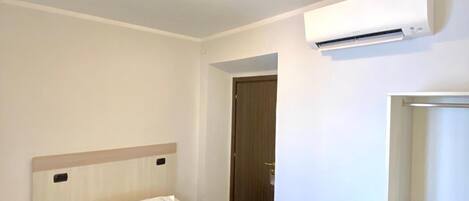 A hotel room with a bed, an air conditioning unit, a wardrobe, and a door.