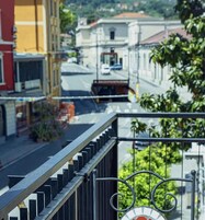Un balcón con barandilla de metal que da a una calle con edificios y un coche aparcado.
