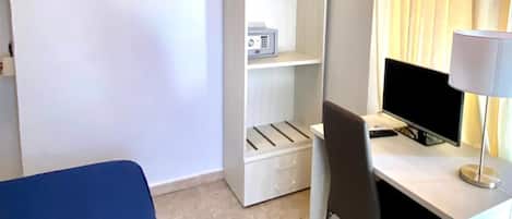 Una habitación de hotel con cama, escritorio con computadora, silla, armario y aire acondicionado.