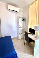 Una habitación de hotel con cama, escritorio con computadora, silla, armario y aire acondicionado.