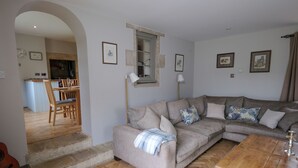 Un salon avec un canapé d’angle beige, une table basse en bois et un parquet à motifs chevrons.