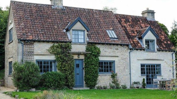 Une maison en pierre avec un toit en tuiles, une porte d’entrée et un petit jardin.