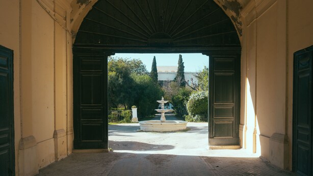 An arched doorway leading to a courtyard with a fountain and trees. - L'appartement du Palais (La Marsa)