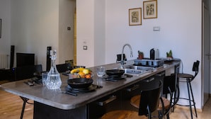 A modern kitchen with a central island, black chairs, a sink, and a dining area. - L'appartement du Palais (La Marsa)