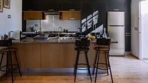 A modern kitchen with a central island, bar stools, and a stainless steel refrigerator. - L'appartement du Palais (La Marsa)
