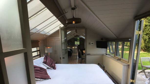 Un dormitorio con una cama grande, un escritorio y un televisor. Hay una ventana y una puerta que da a otra habitación.
