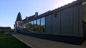 Un edificio con una larga pared lateral con ventanas amplias, un camino de grava y una zona ajardinada.