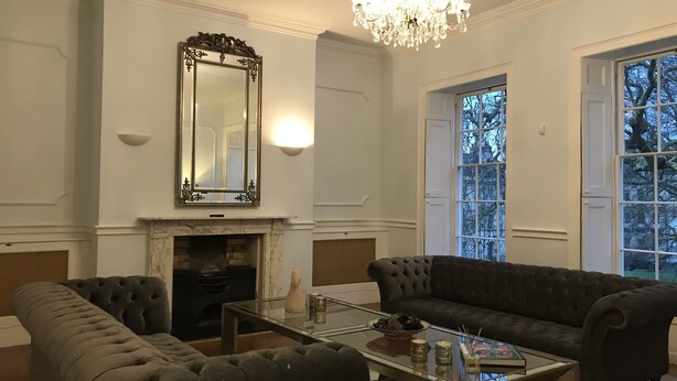 Ein Wohnzimmer mit Kamin, zwei dunklen Sofas, einem Glastisch und einer Chandelier.