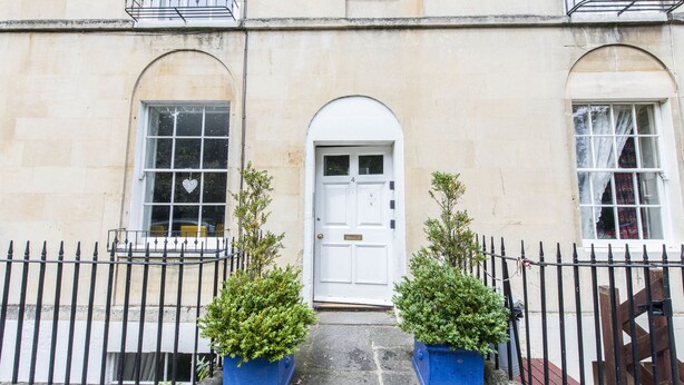 A building with a white door, two windows with heart-shaped decorations, and a black iron fence. - Maises's Maisonette (Bath)