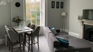 A dining area with a table and chairs, a sofa, a fireplace, and a television. - River View (Bath)