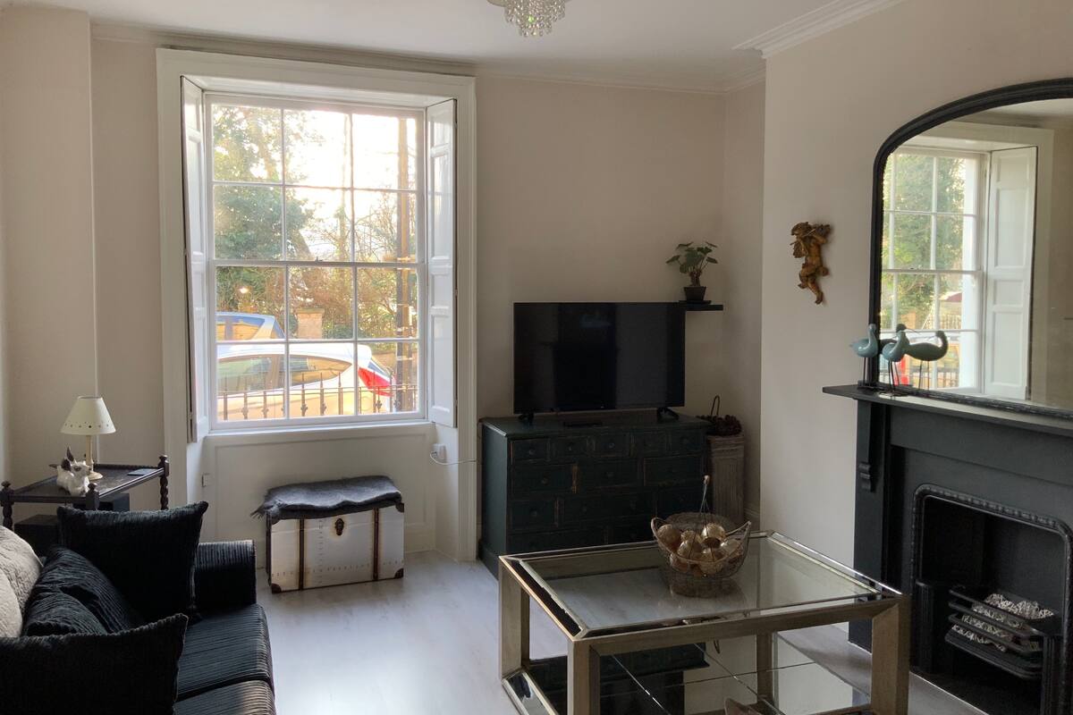 A living room with a sofa, a glass coffee table, a television, a fireplace, and a large window with a view of the outside.