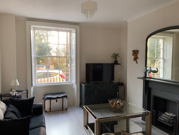 Una sala de estar con sofá, mesa de centro de vidrio, televisor, chimenea y un ventanal con vistas al exterior.