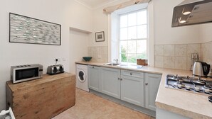 A modern kitchen with a built-in washing machine, a microwave, a toaster, a sink, and a gas stove. - Gilda's Garden (Bath)