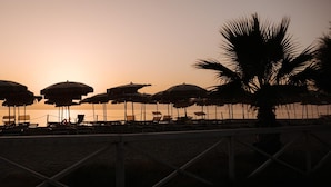 A beach with rows of sun umbrellas and lounge chairs, a palm tree, and a sunset in the background. - Hotel Residence Solemare (Ricadi)