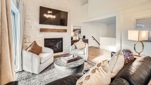Ein modernes Wohnzimmer mit Kamin aus Stein, zwei Sofas, einem Couchtisch und einem an der Wand montierten Fernseher.