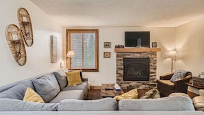 Una sala de estar con un sofá seccional gris, una chimenea de piedra y un televisor montado encima.