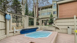 Una terraza de madera con un jacuzzi, una valla de madera y un edificio al fondo.