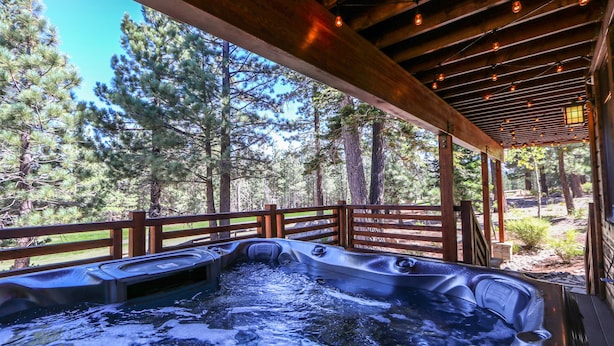 Un bain à remous installé sur une terrasse en bois à l’extérieur, avec vue sur des pins.
