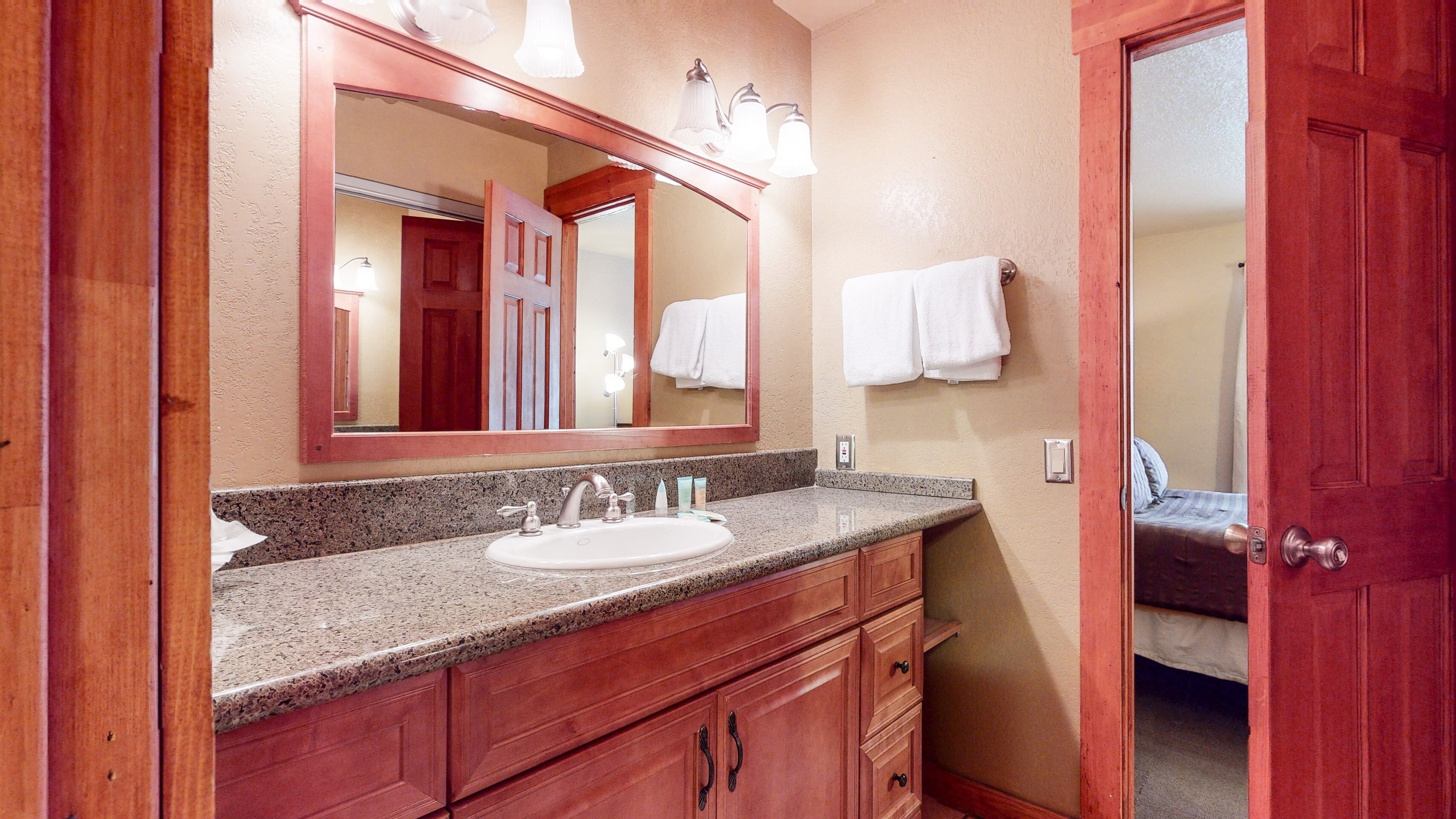 A bathroom with a granite countertop, a sink, a mirror, and wooden cabinets.