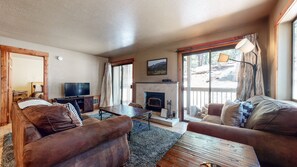 A cozy living room with a fireplace, comfortable seating, a television, and a view of the outdoors.