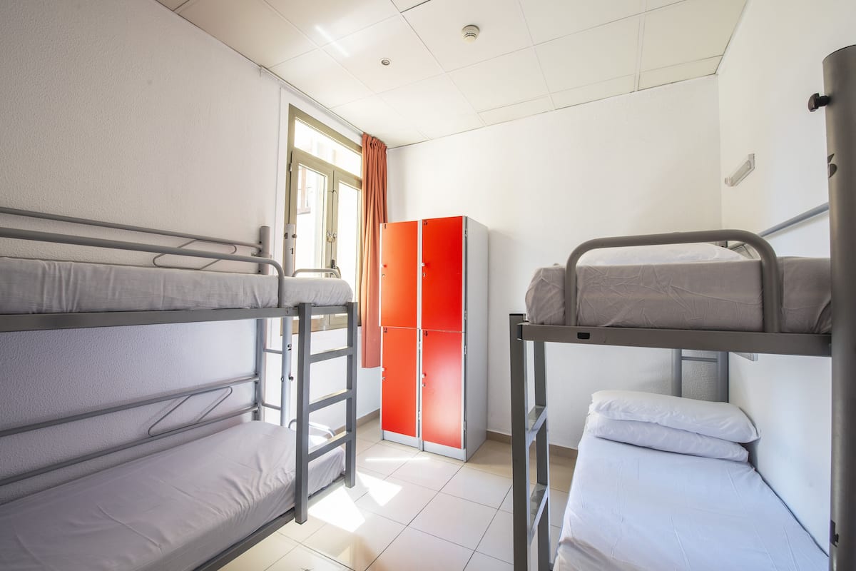 A dormitory room with bunk beds, a wardrobe, and a window with curtains.