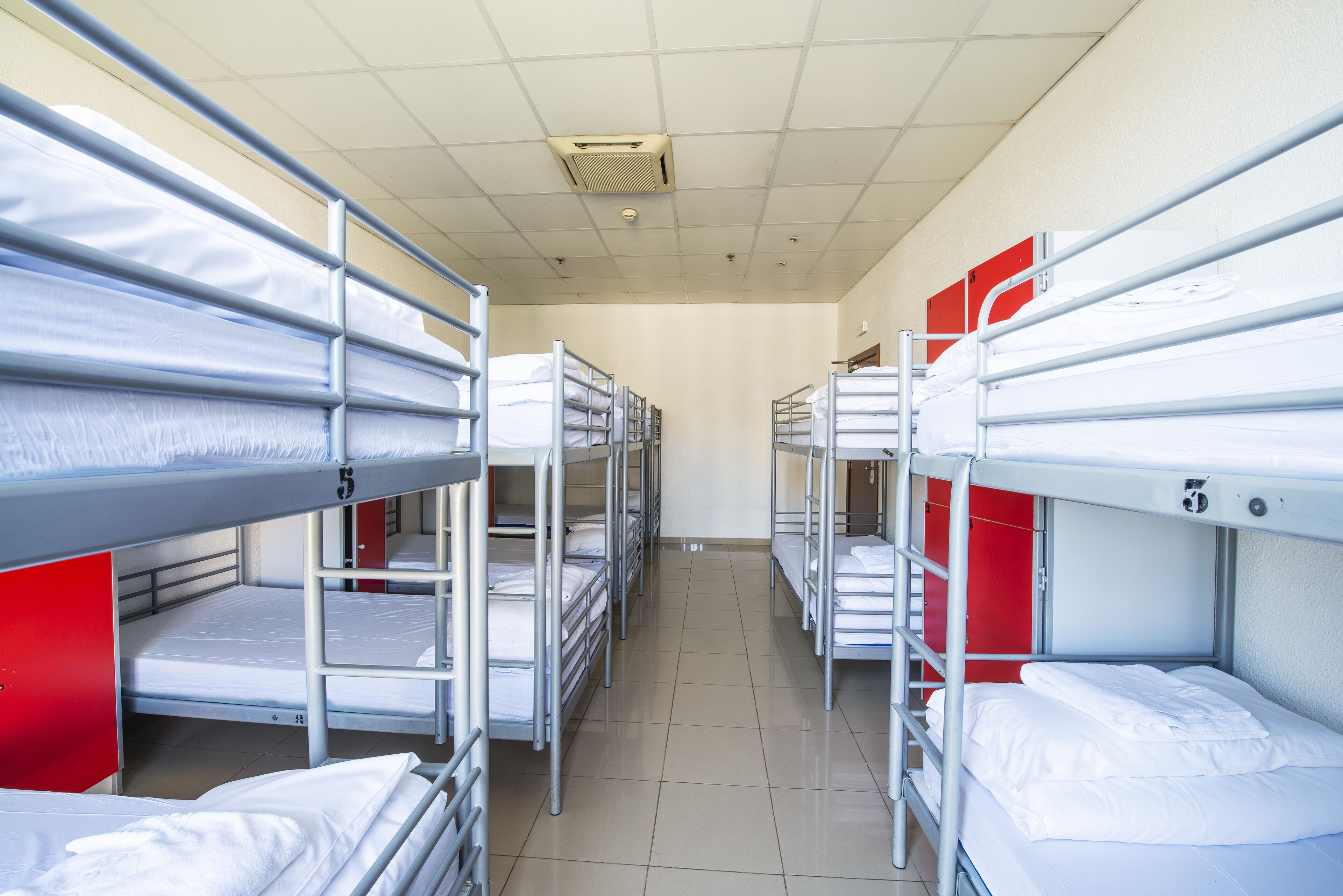 A row of bunk beds in a dormitory room with a tiled floor and a red accent wall.