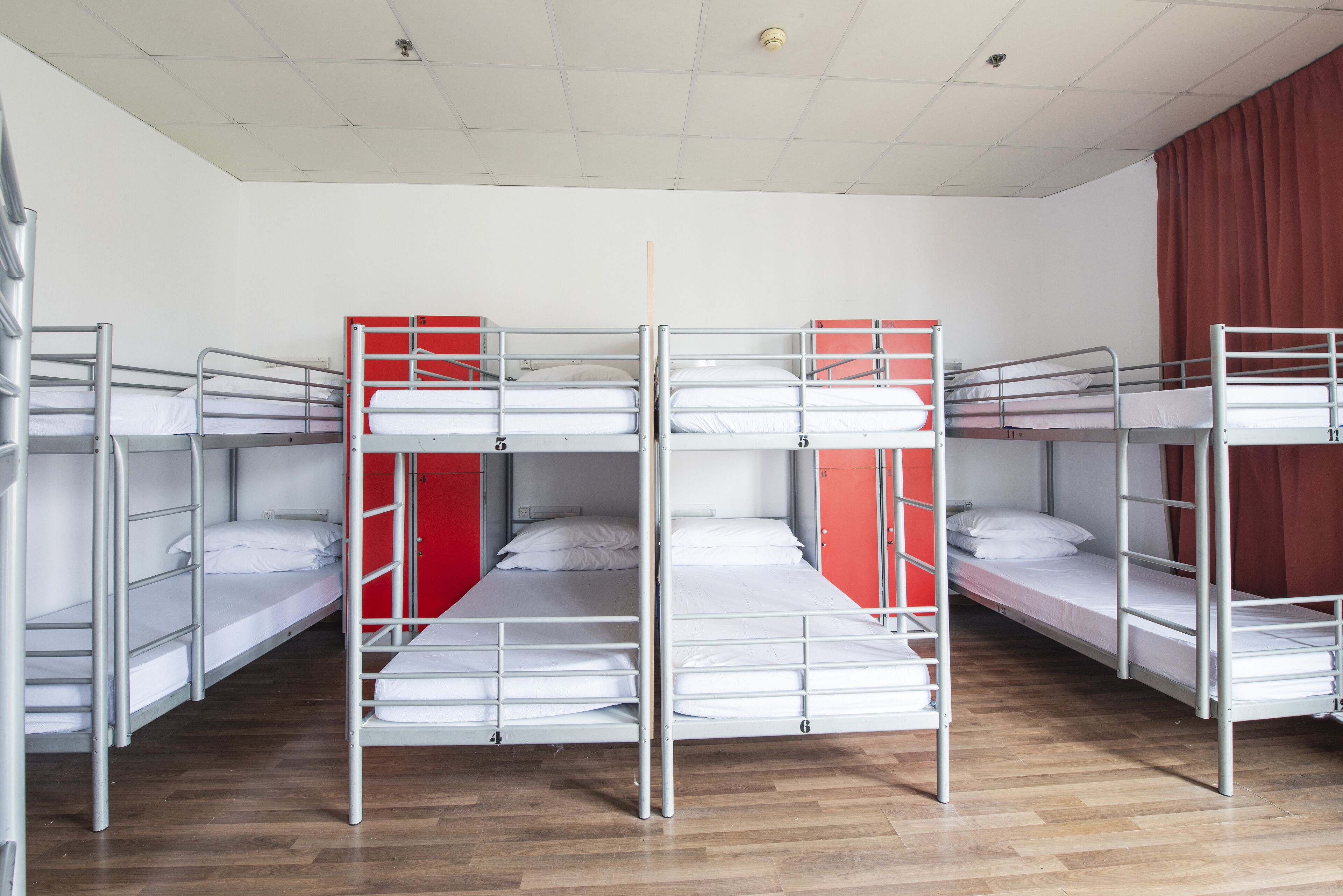 Un dormitorio con literas, suelo de madera y una cortina roja.