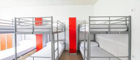 Een slaapzaal met stapelbedden, een rode zuil en een raam met oranje gordijnen.
