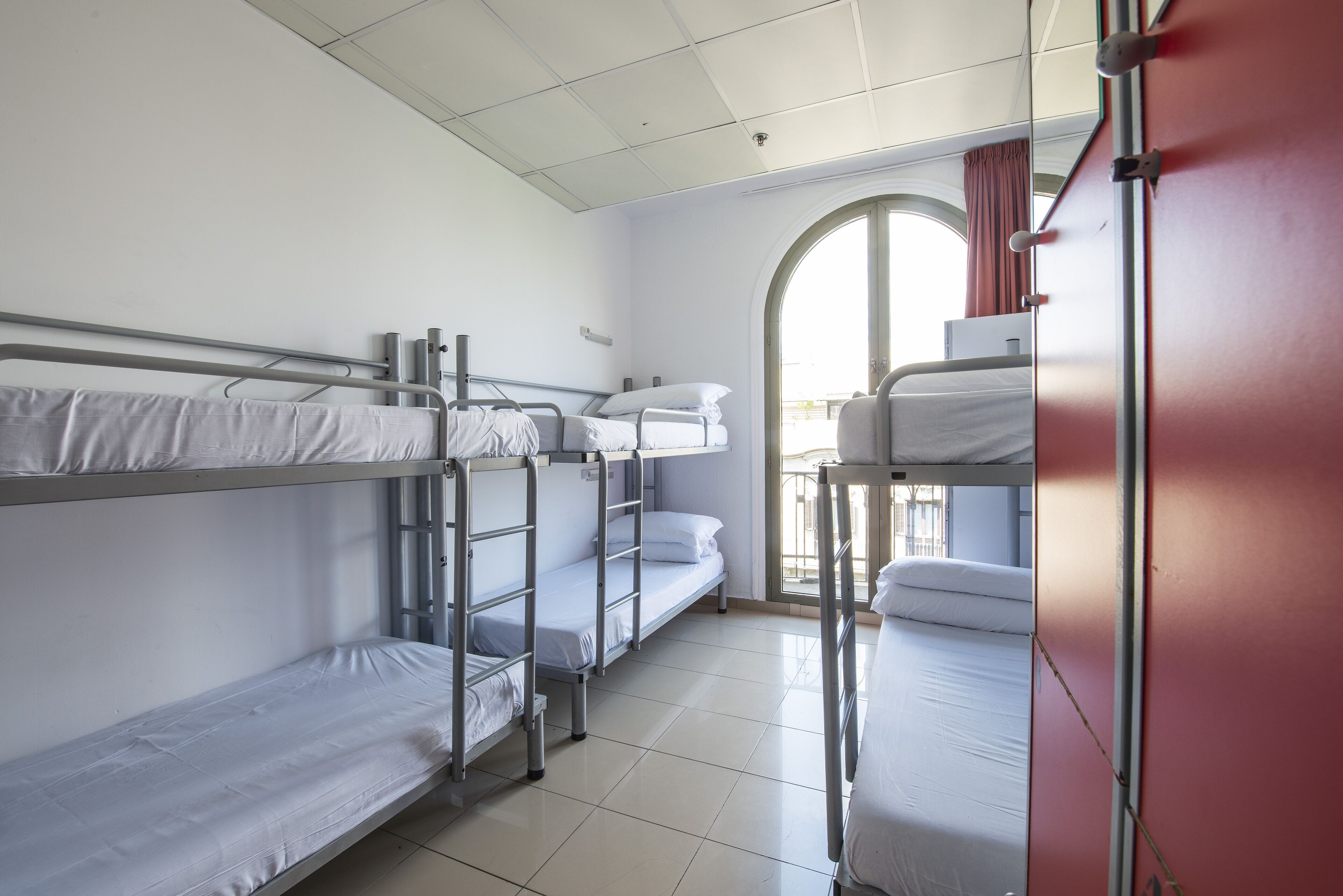 A dormitory room with bunk beds, a window with curtains, and a tiled floor.