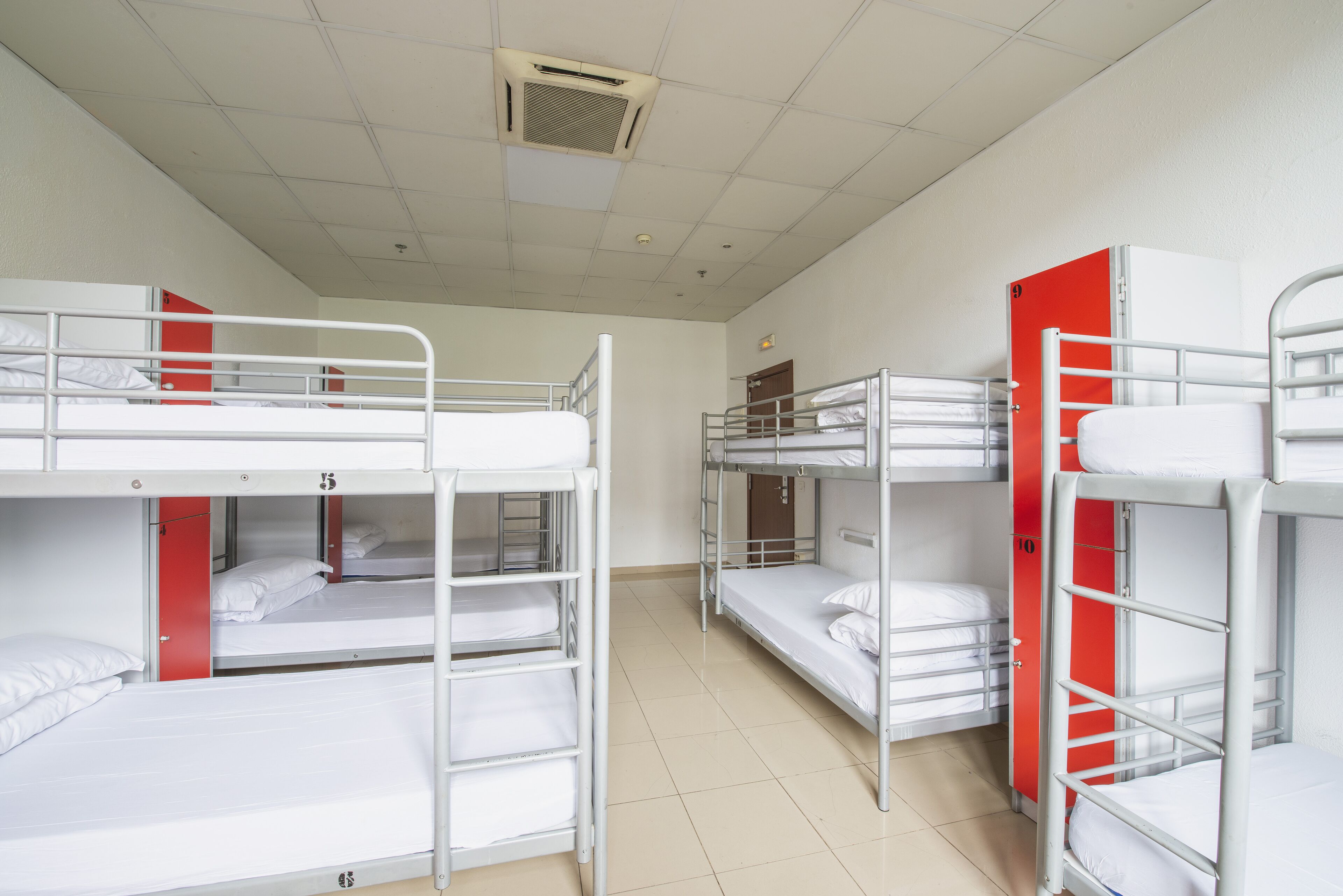 A dormitory room with bunk beds, a red door, and a tiled floor.