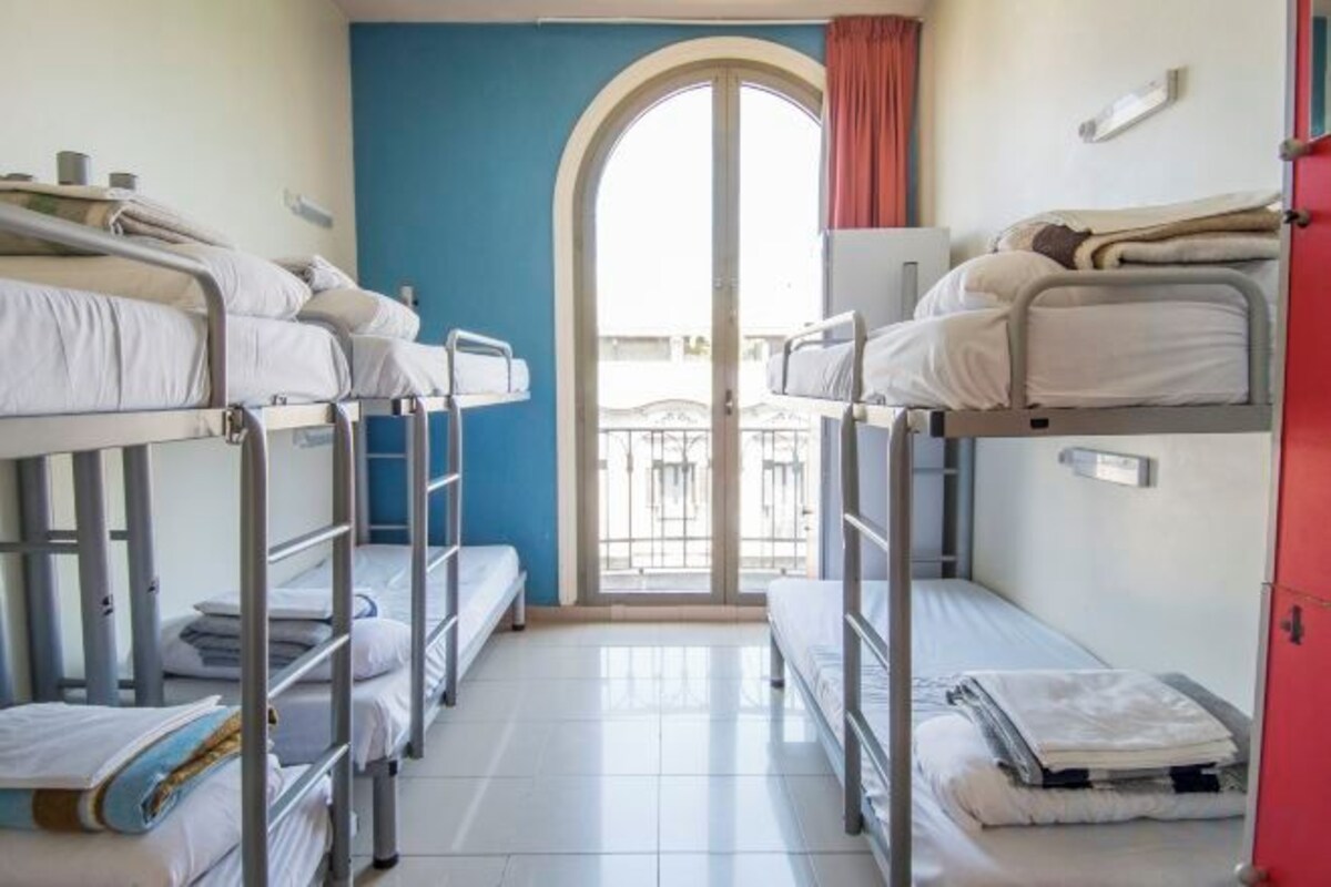 A room with bunk beds, a door leading to an outdoor balcony, and a window with curtains.
