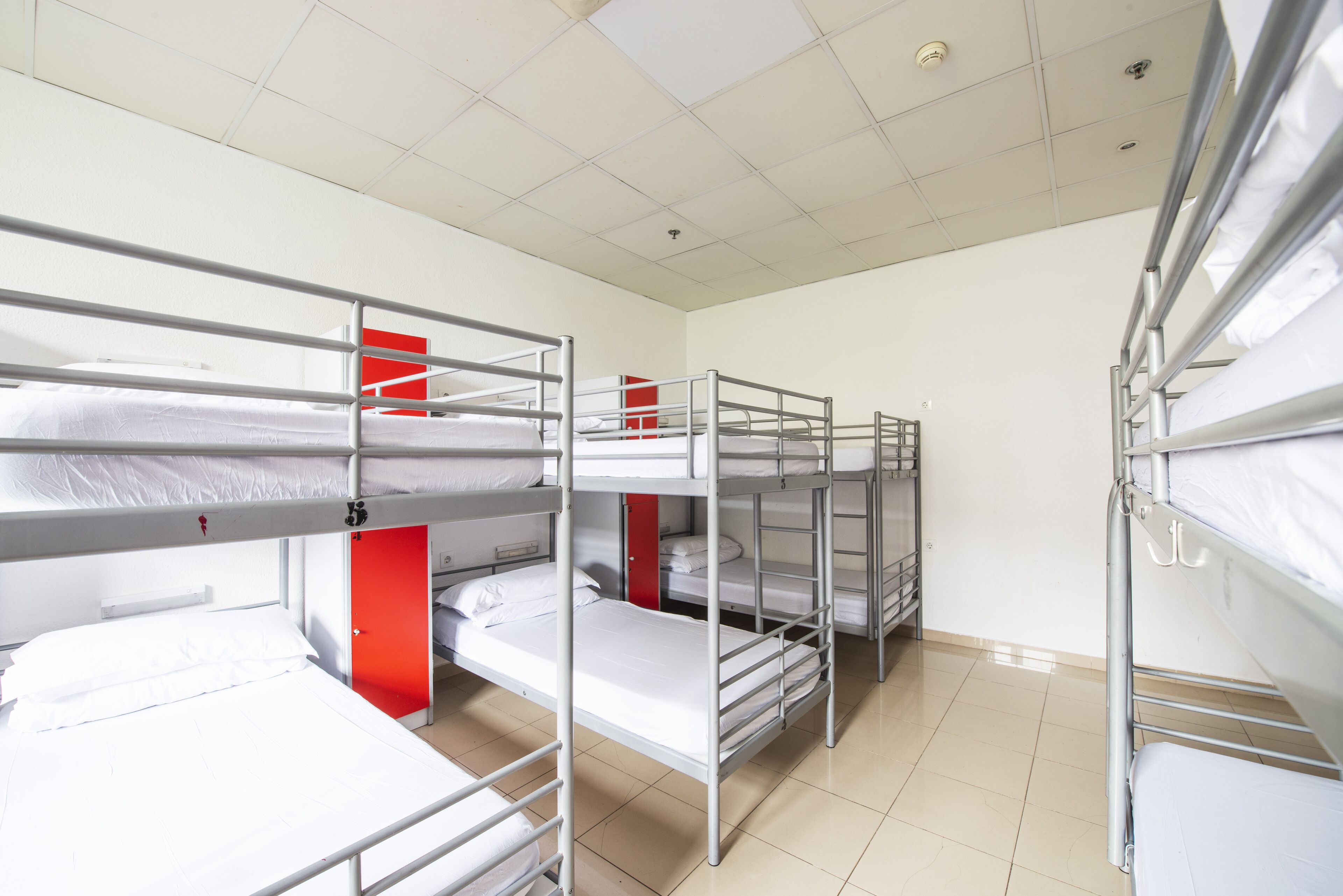 Un dormitorio con literas, una puerta roja y suelo de baldosas.