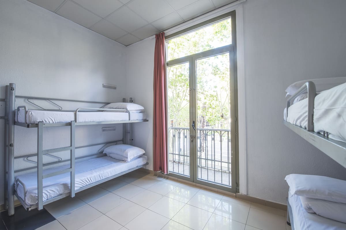A dormitory room with bunk beds, a sliding glass door to the outside, and a tiled floor.