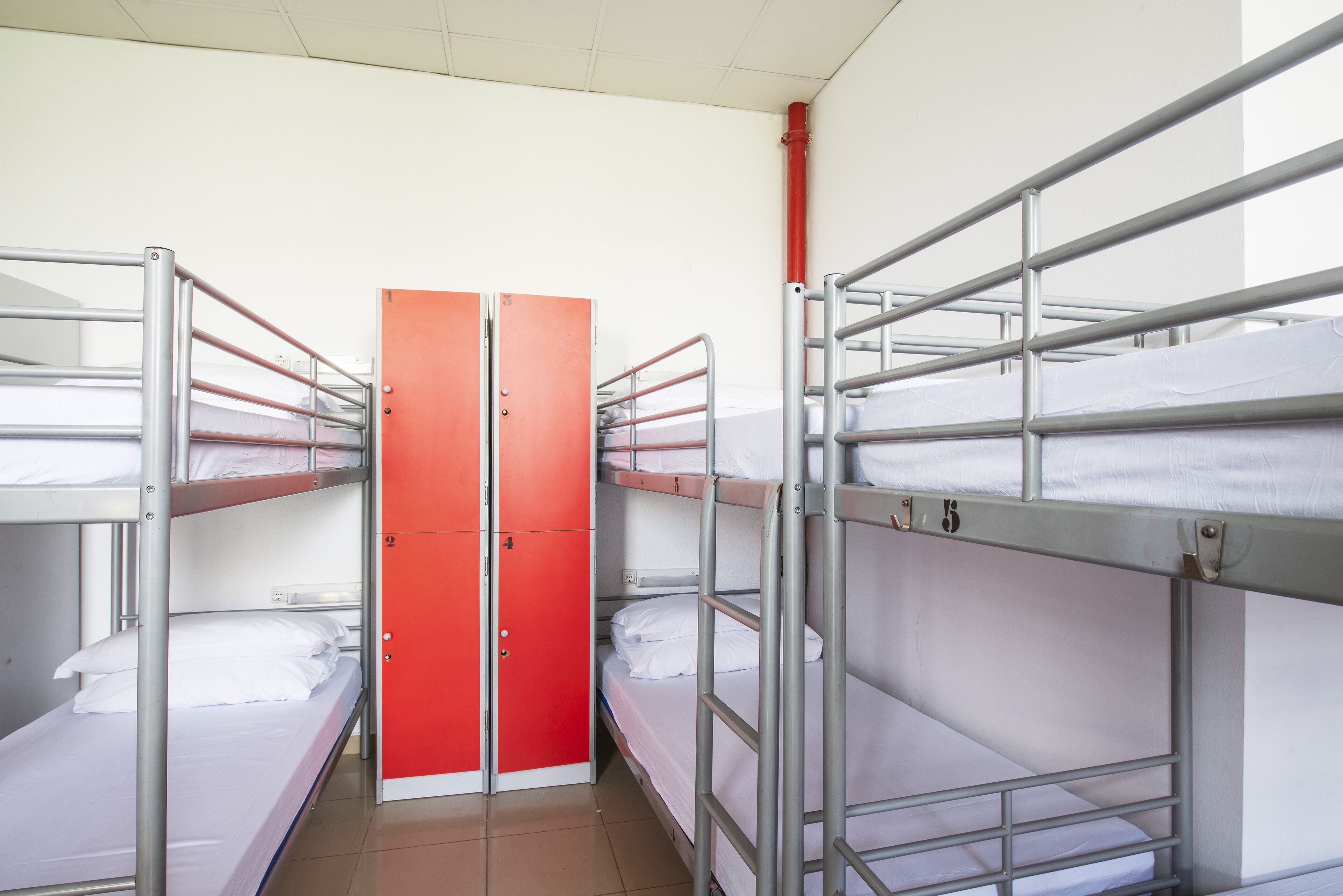 Et sovesal med køjesenge, en rød dør og et hvidt loft.