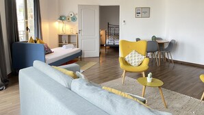 A modern living room with a sofa, a yellow armchair, a dining table with chairs, and a bed with a headboard. - Safestay Barcelona Passeig de Gracia (Barcelona)