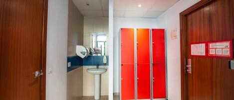 A hallway with a sink, a mirror, and red lockers.