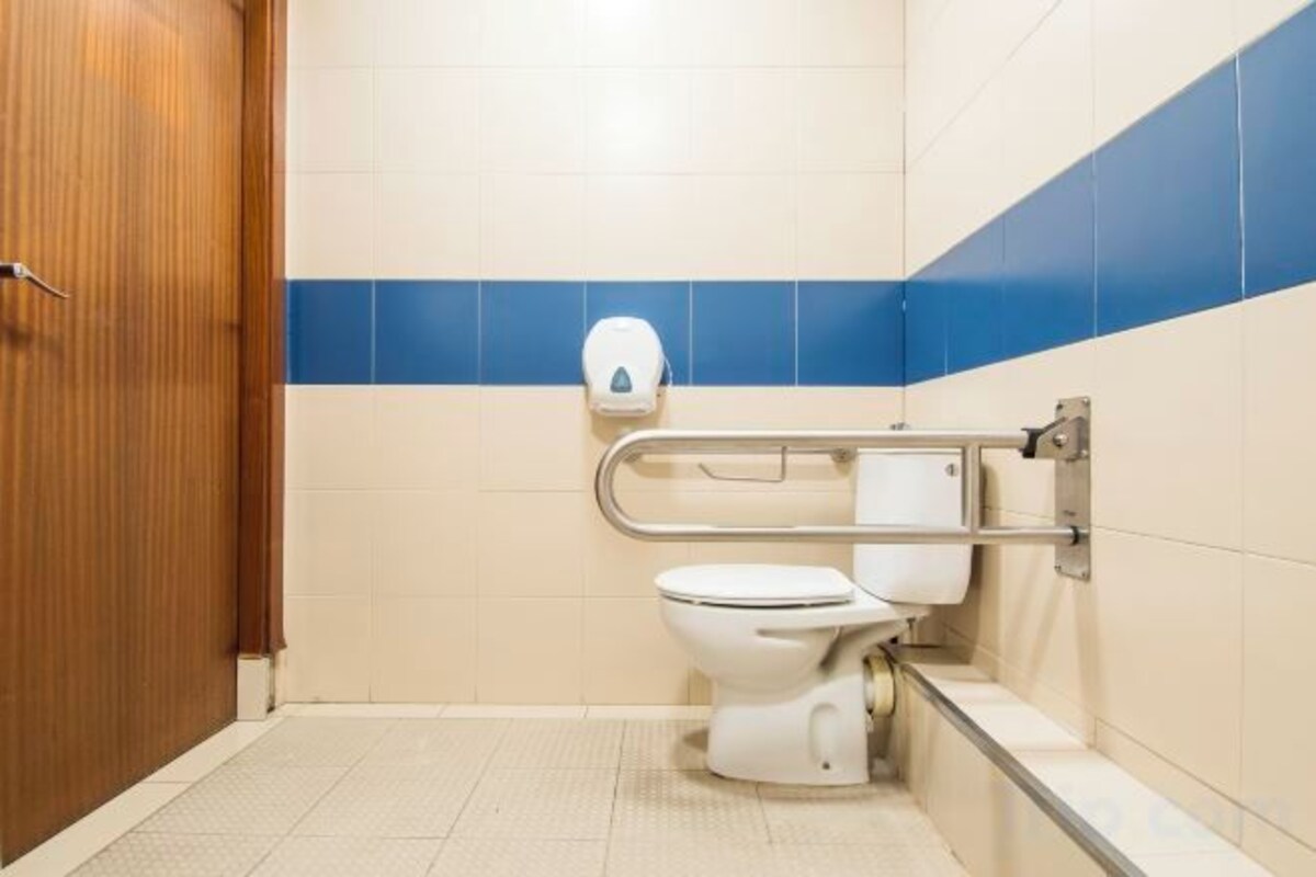 A standard bathroom with a toilet, hand dryer, and grab bars.