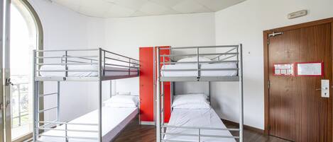 A dormitory room with bunk beds, a wooden door, and a window with a view.